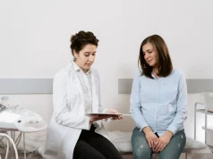PCOS’ta İnsülin Direnci Neden Gelişir ve Nasıl Yönetilir Kadın hekim muayene odasında genç bir kadınla PCOS ve kan şekeri test sonuçlarını konuşuyor