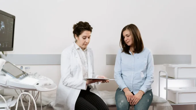 PCOS ve insülin direnci değerlendirmesi Kadın hekim muayene odasında genç bir kadınla PCOS ve kan şekeri test sonuçlarını konuşuyor